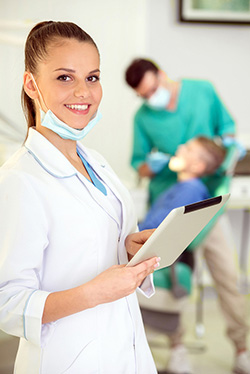 Dental assistant holding a tablet in front of a doctor working with a patient